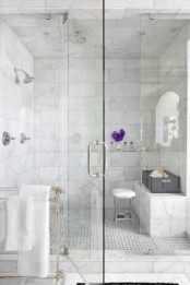 a chic shower space done with marble tiles and matching patterned tiles on the floor plus seamless glass doors