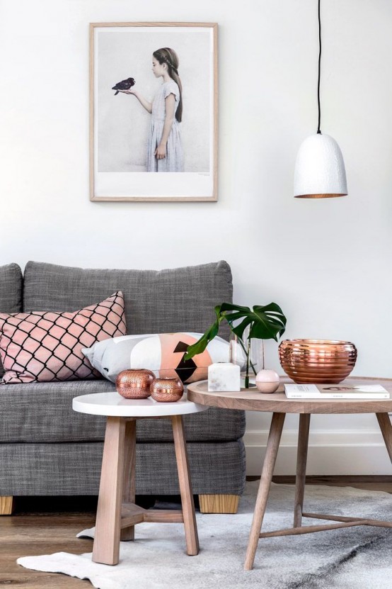 a Scandinavian living room with a grey sofa and pink pillows, round tables, a white pendant lamp and an artwork