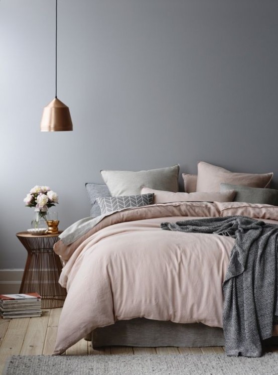 a serene grey bedroom with a bed with blush and grey bedding, a pendant lamp, a wooden stool with books