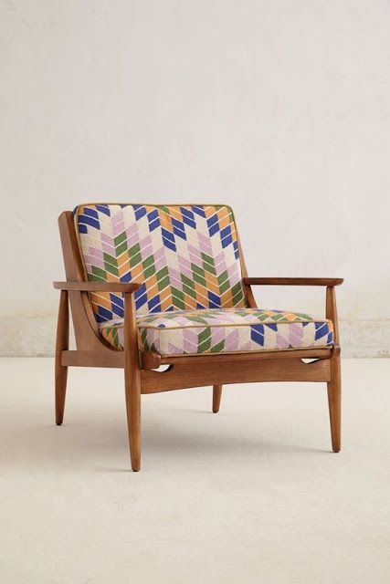 a mid century modern to boho chair with a stained frame, armrests and legs and bright geo printed upholstery
