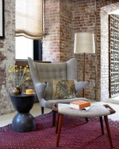 a grey wingback chair with tall armrests and a colorful pillow welcomes to take a seat and relax a little bit
