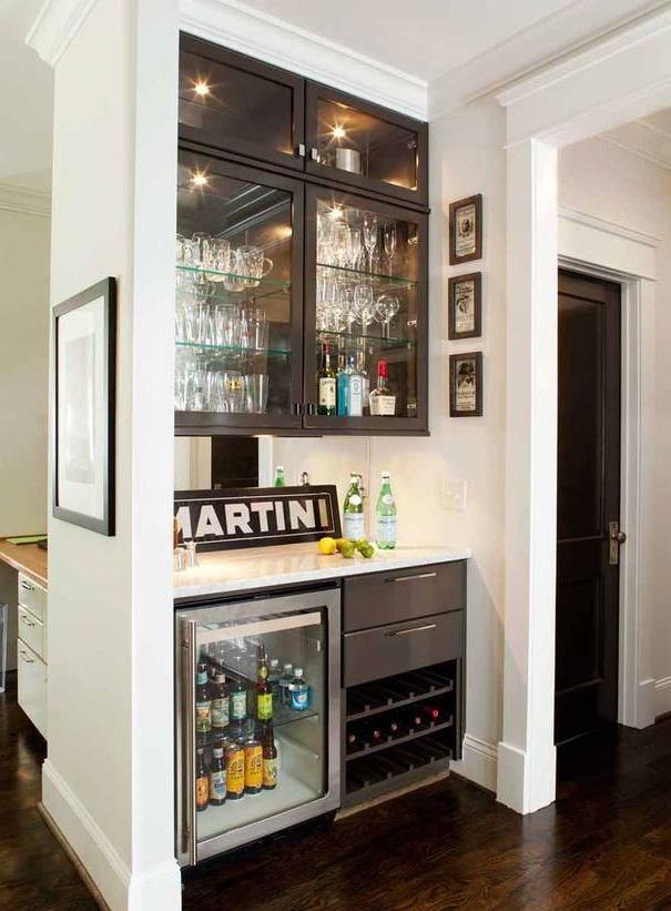 a stylish home bar with several cabinets, a fridge and a mirror backsplash plus a sign is a cool idea