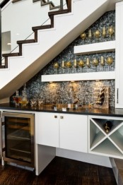 an open under the stairs home bar with a mosaic silver tile backsplash, open shelves and a fridge plus a cabinet and built-in lights