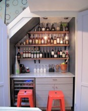 a home bar under the stairs, with open shelves, bulbs, a cabinet and a small fridge for drinks plus colorful stools