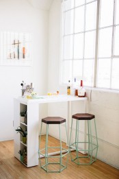 a white mini bar with a space to sit, with a closed storage compartment and some things on the table and mint stools