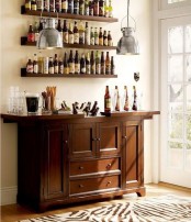 a vintage wooden bar and matching shelves over it to organize a whole home bar in the space