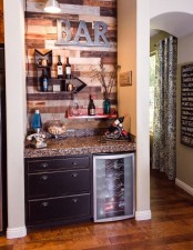 a small rustic home bar with a wood clad wall, open shelves, a cabinet and a fridge plus built-in lights