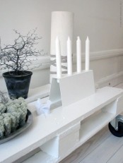 white candles in a white candle holder, black branches in a pot and some moss for an ultra-minimal holiday look