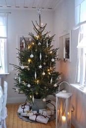 a natural minimalist Christmas tree with metallic and white ornaments and lights plus candle lanterns