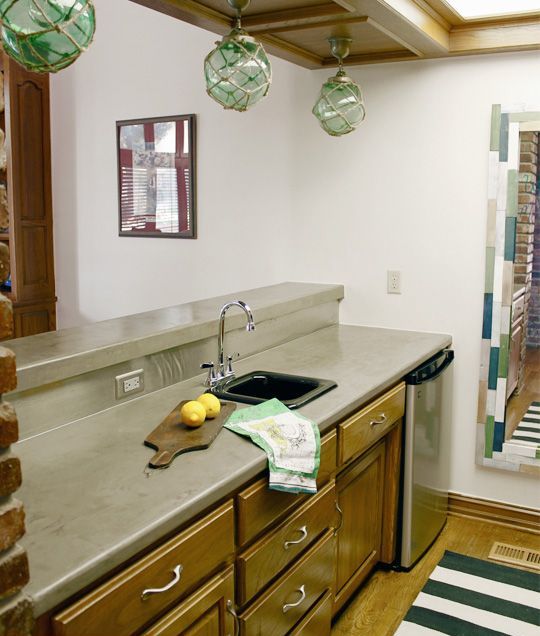 a modern kitchen wiht brown cabinets and a concrete countertop plus floats over the cabinets for a coastal look
