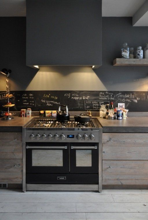 a chic industrial kitchen with wooden cabinets and concrete countertops, with a chalkboard backsplash and a large hood with lights