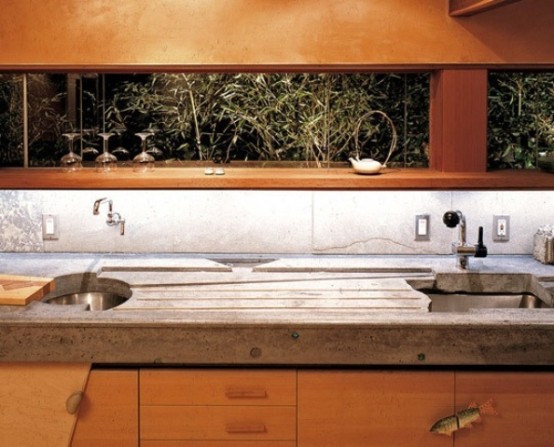 a peaceful kitchen of light-colored wooden cabinets with a window backsplash and concrete countertops