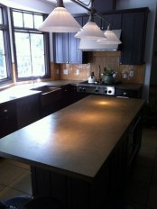 a dark farmhouse kitchen with concrete countertops, a brown tile backsplash and vintage lamps