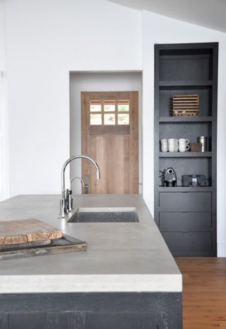 a minimalist monochromatic kitchen with white walls, black cabients and a black kitchen island with a concrete countertop