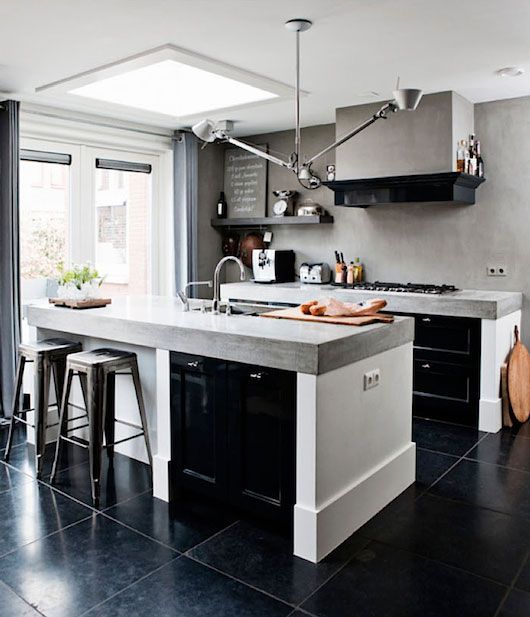 a stylish modern kitchen with black and white cabinets, a concrete backsplash and countertops, a metal lamp and metal stools