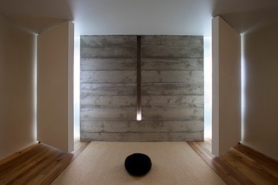 a minimalist meditation space with a wooden wall, a wall lamp, a rug and pillows