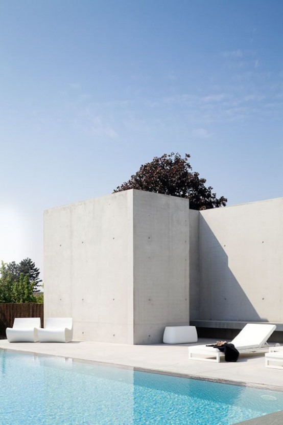 a minimalist terrace with a concrete deck and concrete walls, very minimal white outdoor furniture and a pool is a lovely space to be