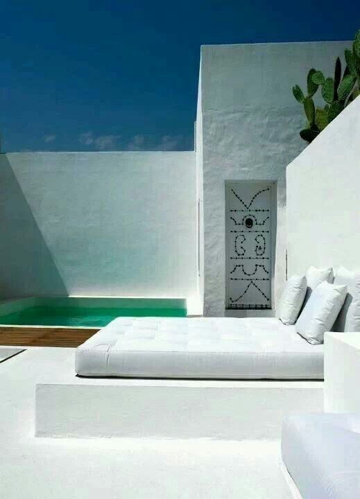 a minimalist white terrace with a small pool, a built-in bed and seats, a decorated niche and a mattress with pillows is a very laconic space