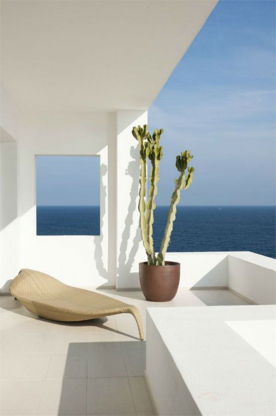 a minimalist terrace with tiles on the floor, a woven daybed and a cactus in a planter plus a fantastic sea view