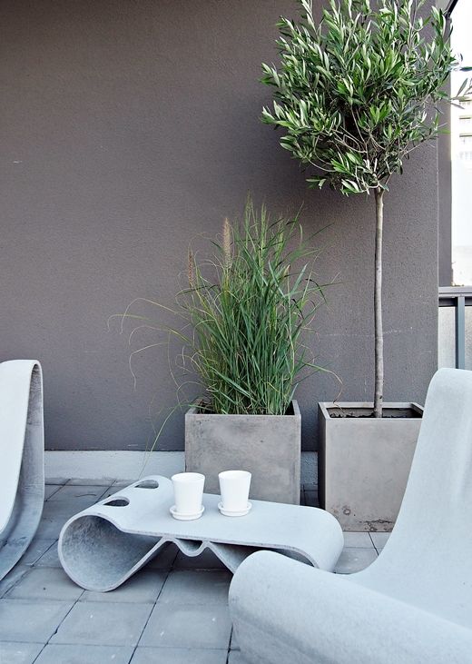 a minimalist terrace clad with concrete tiles, with sculptural concrete furniture and potted grasses and a tree in concrete planters is very chic