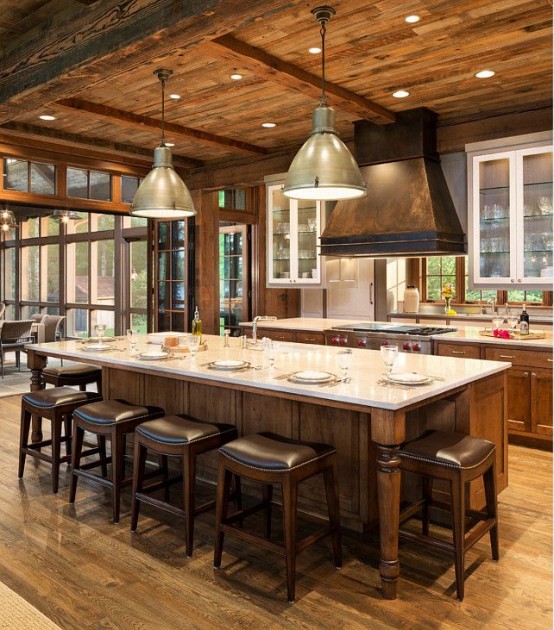 a beautiful chalet kitchen with wooden cabinets, walls, ceiling and beams, a large kitchen island in vintage style and dark leather stools for eating here