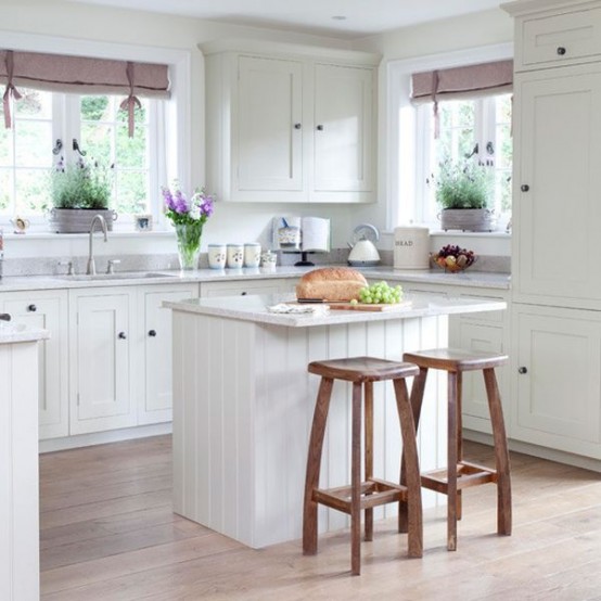 a white cottage kitchen with a white stone countertop, a small planked kitchen island with stools and lilac touches for a cuter look