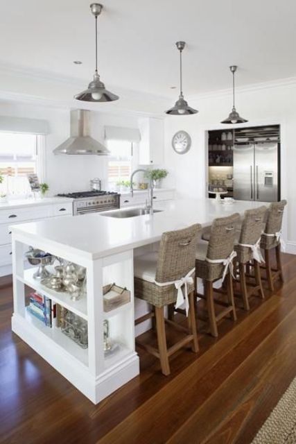 a white farmhouse kitchen with elegant cabinetry, a large white kitchen island with an open storage shelf and a seating space with tall woven stools