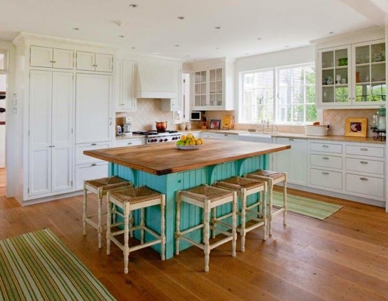 a white farmhouse kitchen with a contrasting turquoise kitchen island that doubles as a dining table and green striped rugs all around