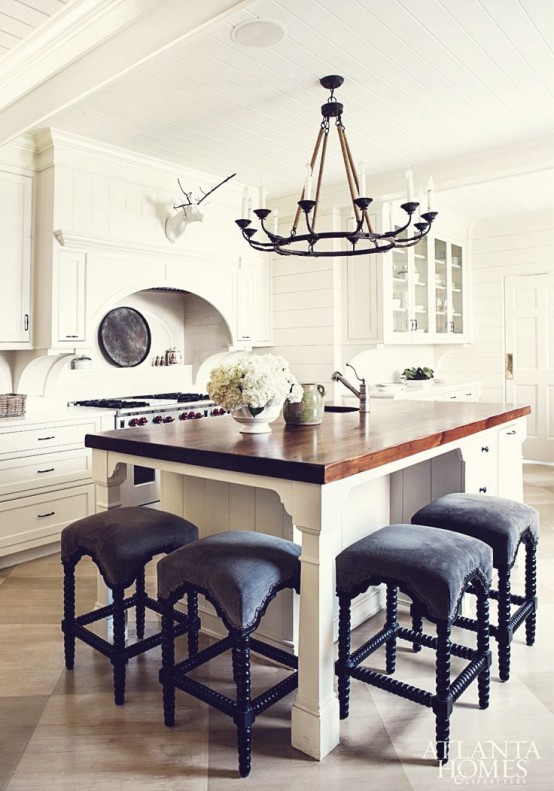 a white farmhouse kitchen with shaker style cabinets, a small kitchen island with a seating space and black stools plus a black vintage chandelier