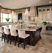 a chic vintage kitchen with neutral cabinets, a whitewashed hood, crystal chandeliers, a dark stained kitchen island with an eating space and tall stools