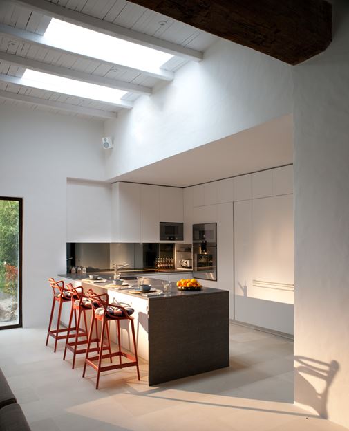 a minimalist white kitchen with sleek cabinets, a grey kitchen island and red stools for a contrasting touch
