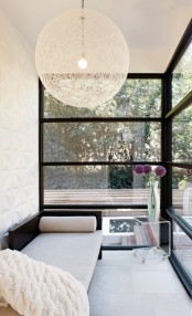 a neutral modern sunroom with glazed walls, a black daybed with pillows and a blanket, an acrylic side table, a pendant lamp is amazing