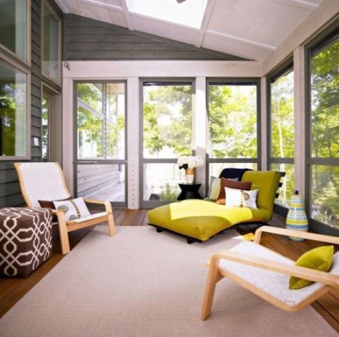 a small modern sunroom with series of windows, Scandi chairs, a green and yellow lounger, side tables and a printed pouf and a skylight for natural light