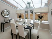 a modern neutral sunroom as a dining space, all tan everything, a black console table and a black table, neutral chairs, a glass roof for maximal natural light