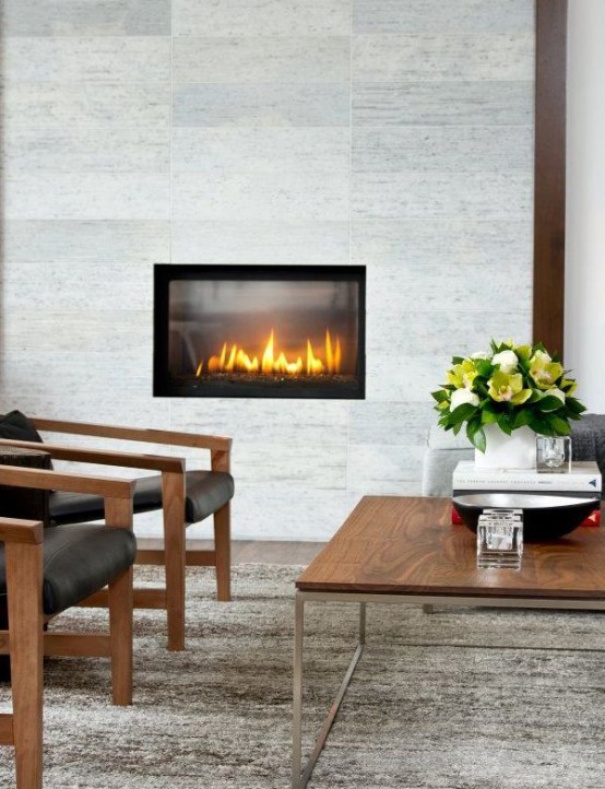 an elegant neutral living room with a built-in fireplace and stone tiles around, a low coffee table and black leather chairs plus blooms