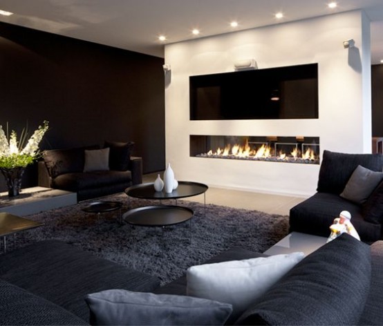a bold black and white living room with a black accent wall, black seating furniture, a duo of black coffee tables, a built-in fireplace and a TV over it