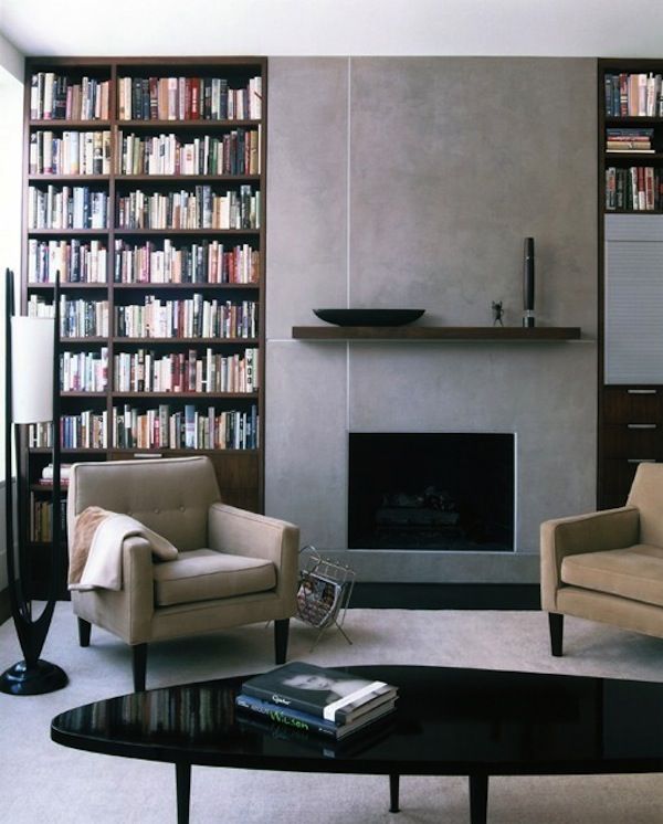 an elegant modern living room with a built in fireplace with a concrete surround, built in bookshelves, neutral chairs, a low black coffee table is a chic and lovely space to be in