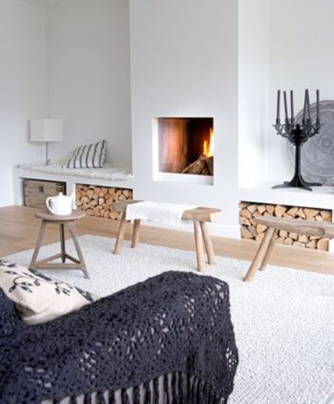a stylish and welcoming Scandinavian living room with a built-in fireplace and firewood storage niches that double as benches, a sofa with a dark cover and some small stools and benches