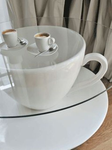 a creative coffee table shaped as an oversized coffee cup with a glass tabletop will fit many living rooms and other spaces