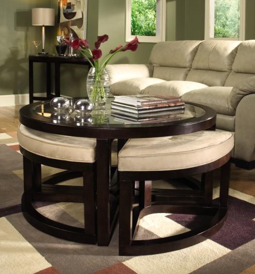 a dark-staiend round coffee table with a glass tabletop and matching poufs under it to create a seating whenever needed