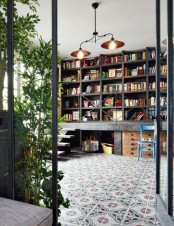 a modern industrial home library done with metal shelves on a raised metal platform, colorful chairs and a metal chandelier