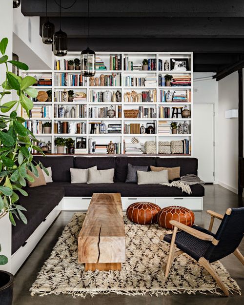 a modern black and white library with white bookshelves, an L-shaped black sofa, a wooden slab table and a black chair