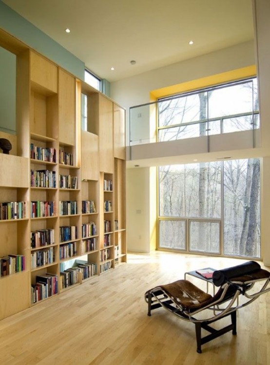 a modern and sleek library done in neutrals, with lots of bookshelves, a double-height window and a comfy lounger