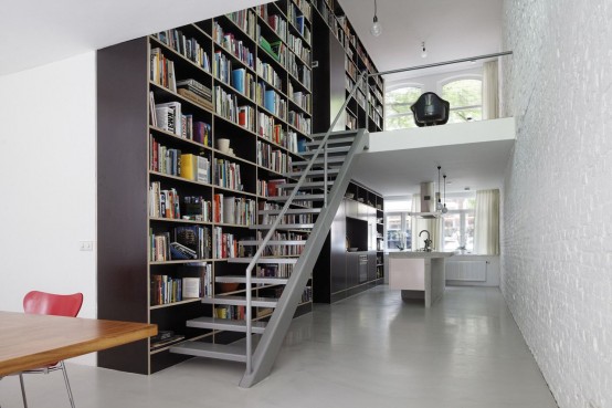 a modern home library on the go - an oversized dark bookshelf unit that is placed on the left of the steps and takes two floors