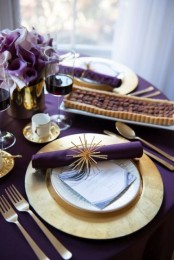 a bold modern Thanksgiving tablescape with a purple tablecloth and napkins, gold chargers, cutlery and saucepans and deep purple blooms