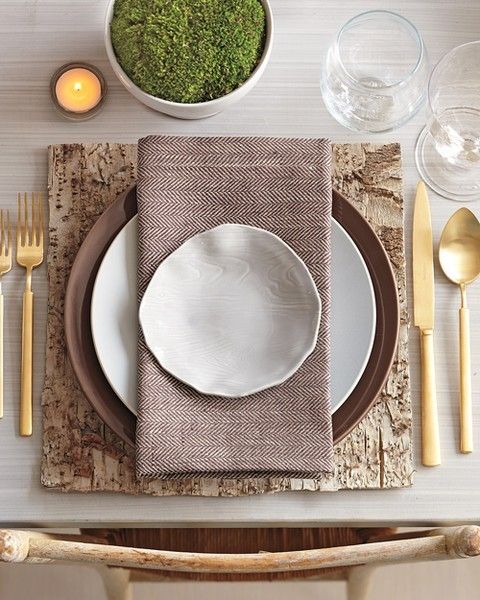 a modern farmhouse Thanksgiving tablescape with a bark placemat, gold cutlery, candles and moss in a planter
