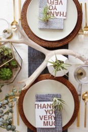 a modern Thanksgiving tablescape with succulents in a terrarium, greenery, antlers, woven chargers and gold cutlery is super chic