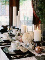 an elegant and contrasting Thanksgiving tablescape with brown placemats and a table runner, gilded pumpkins and candles in glasses is chic