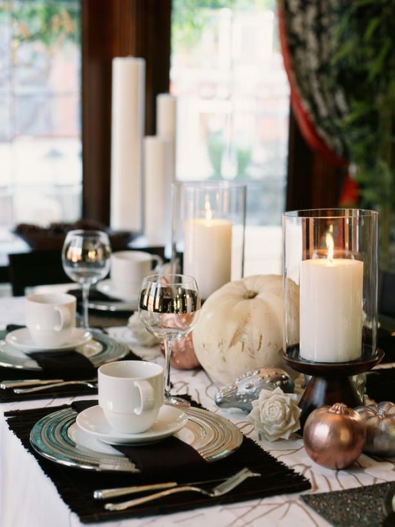 an elegant and contrasting Thanksgiving tablescape with brown placemats and a table runner, gilded pumpkins and candles in glasses is chic