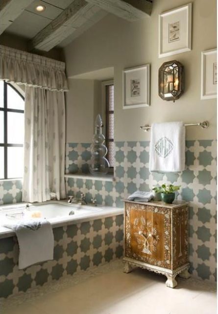 a neutral bathroom with tan walls, beautiful green and creamy Moroccan tiles covering the tub and the walls, vintage furniture and curtains